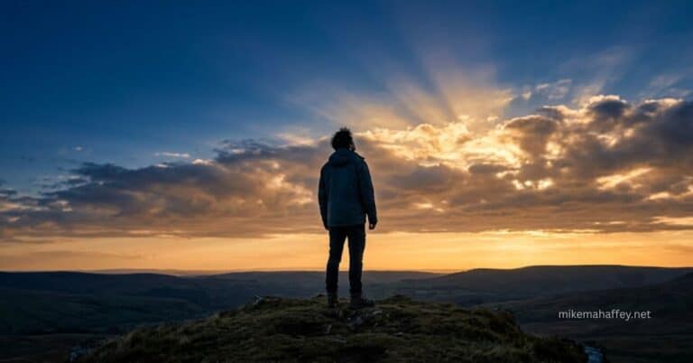 A lone figure stands on a hilltop looking upward toward dramatic rays of golden light breaking through storm clouds over a vast landscape, illustrating the biblical call to set your affection on things above and live with a spiritually minded focus on God.