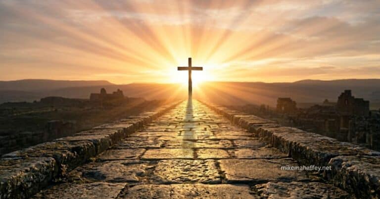 A wooden cross stands at the end of an ancient stone path silhouetted against a blazing sunrise with rays spreading across the sky, illustrating the cross of Christ as the single object and source of saving faith.