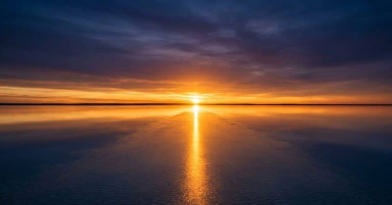 A blazing sunrise reflects across perfectly still water in a long column of golden light stretching toward the viewer, illustrating the new life that breaks through when a believer dies to self and lives with Christ.