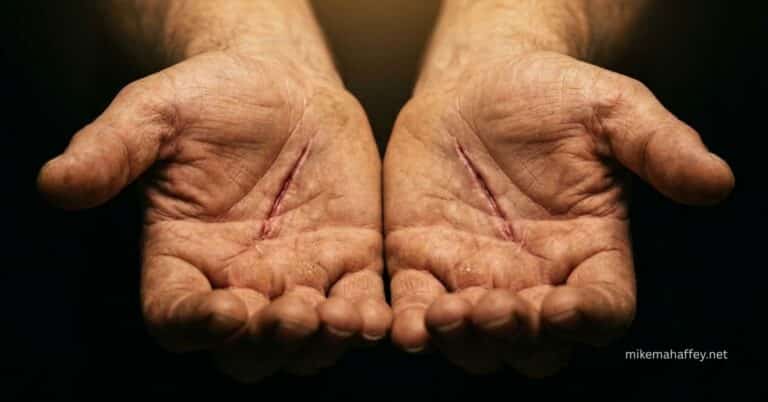 Two open hands held palms upward against a dark background, each bearing a visible nail scar, offering everything accomplished at the Cross to answer the question of what did Jesus accomplish on the cross.