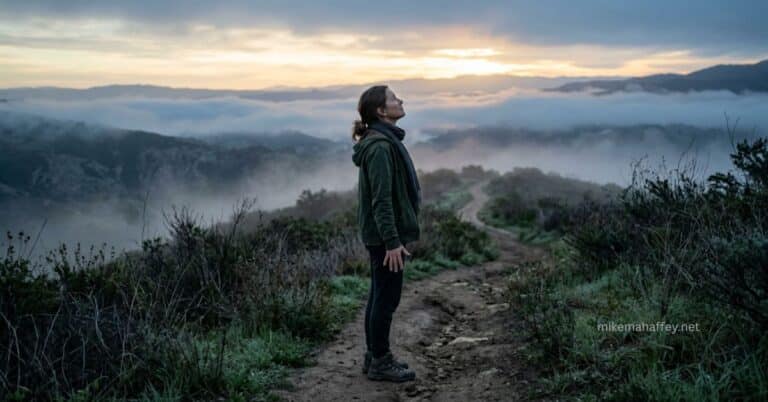 A person stands on a misty mountain path at dawn, face lifted toward the sunrise, arms relaxed at their sides — a picture of the quiet strength the Holy Spirit gives a believer to overcome sin.